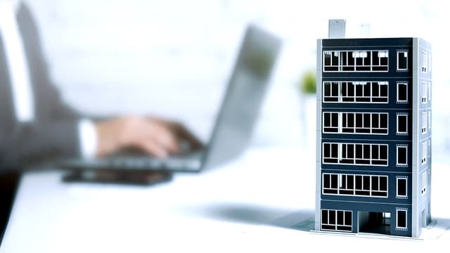 Etualalla kerrostalon pienoismalli jonka taustalla mies tekemässä töitä kannettavalla tietokoneella smartvatten