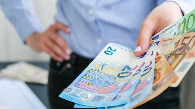 Nainen sinisessä paidassa ojentaa rahaa työ ympäristössä