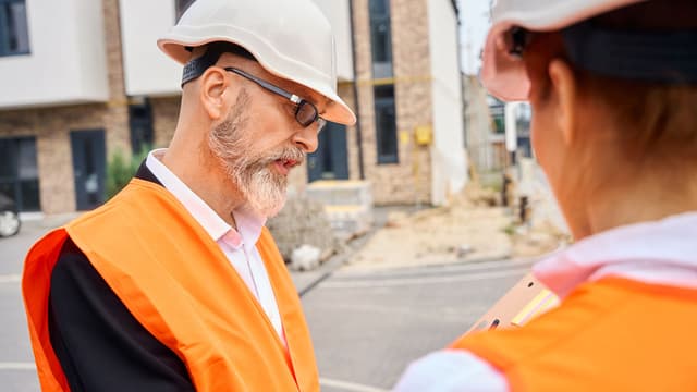 rakennustyömaan henkilökuntaa kypärät päässään katsomassa työmaan papereita