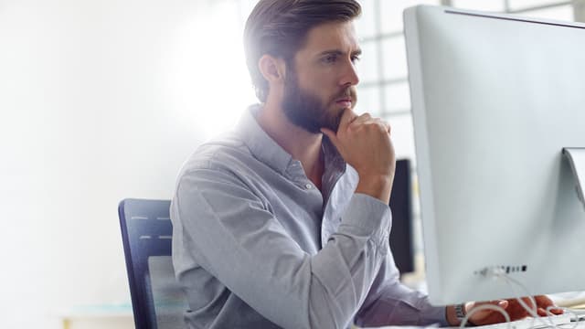 tummahiuksinen mies istuu tietokoneen ääressä ja miettii vaihtoehtoja